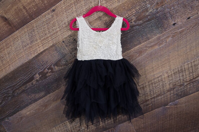 Puede incluir: Un vestido de tul blanco y negro con un corpi&ntilde;o de encaje. El vestido est&aacute; colgado en una percha roja contra un fondo de madera.