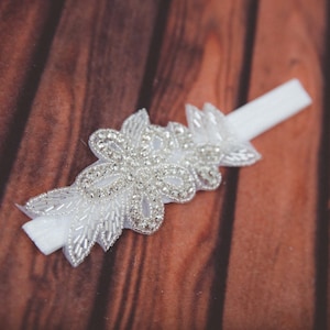 May include: White satin garter with a delicate floral design featuring sparkling rhinestones.