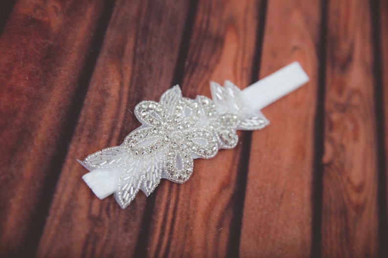 May include: White satin garter with a delicate floral design featuring sparkling rhinestones.