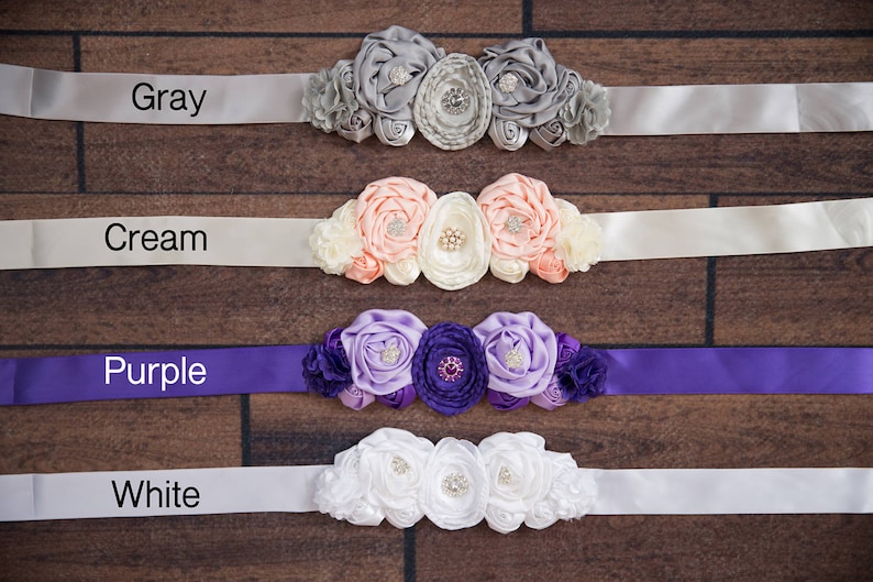 May include: Four satin sashes with different colored ribbons and flower embellishments. The sashes are labeled "Gray", "Cream", "Purple", and "White".