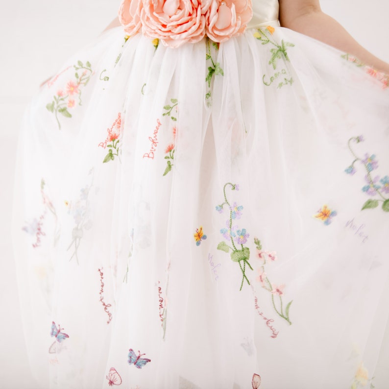 Puede incluir: Falda de tul blanca con bordado floral y las palabras "Birdhouse", "Sweet", "My Daisy", "Violet" y "Forget Me Not".