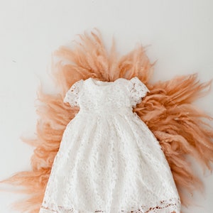 May include: A white lace dress with a scalloped hem, laid out on a peach-colored fluffy surface.