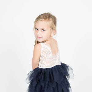 Puede incluir: Una ni&ntilde;a peque&ntilde;a con un top de encaje blanco y una falda de tul azul marino. La falda tiene varias capas y est&aacute; fruncida en la parte inferior.