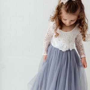May include: A young girl wearing a white lace long-sleeved top with a white flower embellishment and a light blue tulle skirt.