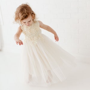 May include: A young girl wearing a white tulle dress with a floral lace bodice. The dress has a flowing skirt and is perfect for a special occasion.