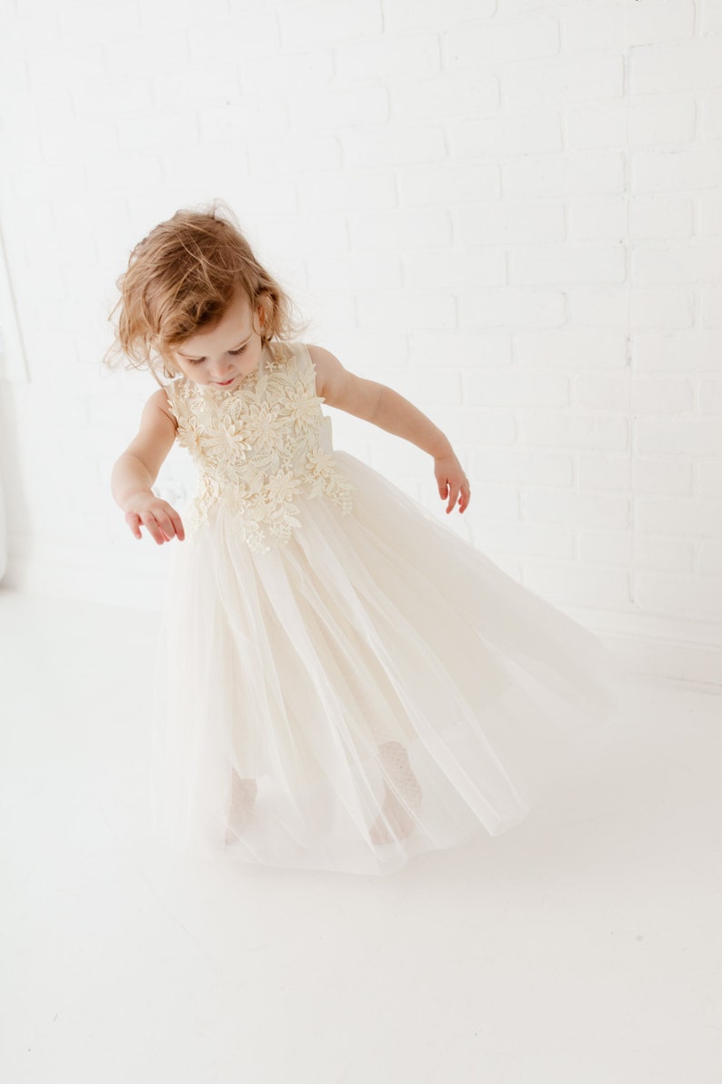 May include: A young girl wearing a white tulle dress with a floral lace bodice. The dress has a flowing skirt and is perfect for a special occasion.