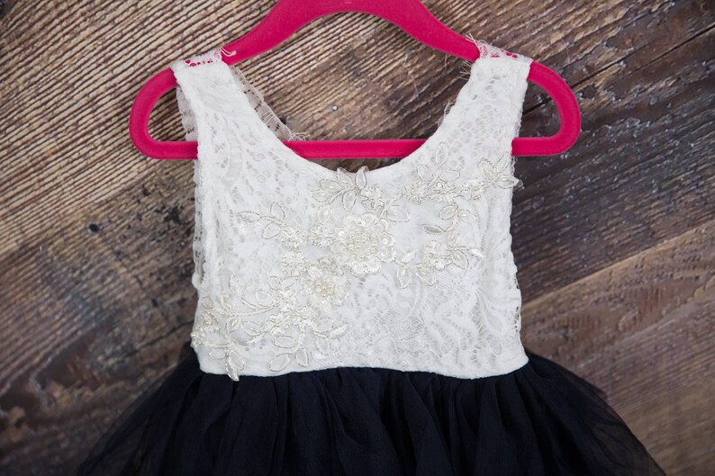 Puede incluir: Un vestido blanco sin mangas de encaje con una falda de tul negro. El vestido est&aacute; en una percha rosa.