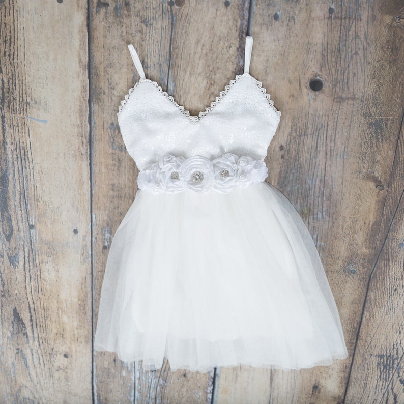 Puede incluir: Vestido de tul blanco con un corpi&ntilde;o de lentejuelas y una faja de flores de sat&eacute;n blanco.