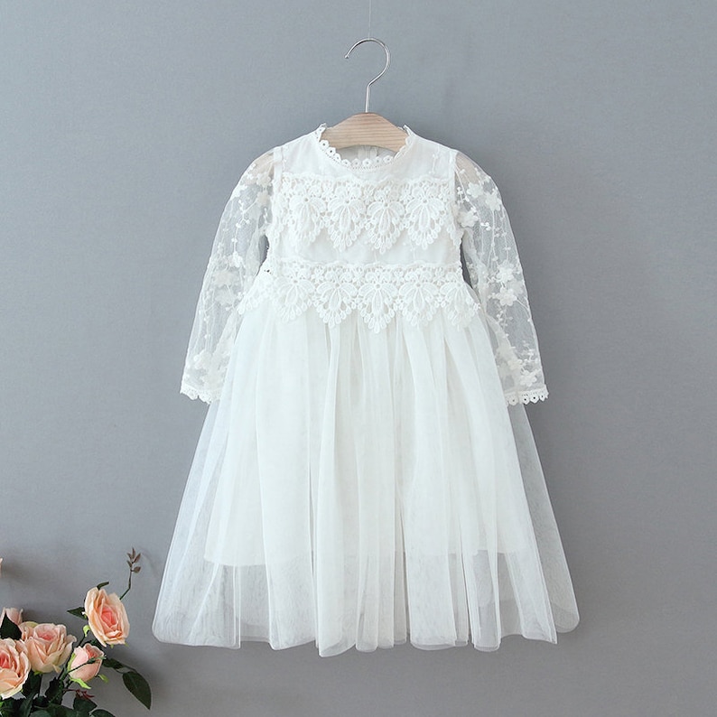 May include: White tulle dress with long sleeves and lace detailing. The dress has a round neckline and a full skirt.