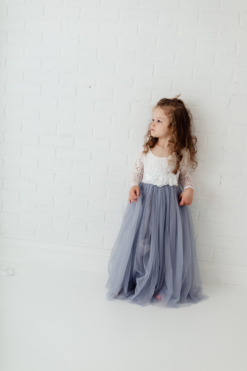 May include: A young girl wearing a white lace top with a long, flowing tulle skirt in a light blue colour. The skirt is gathered at the waist and has a delicate floral design.