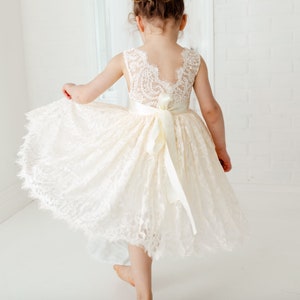 May include: A white lace dress with a satin ribbon sash. The dress has a scalloped hem and a sleeveless design.