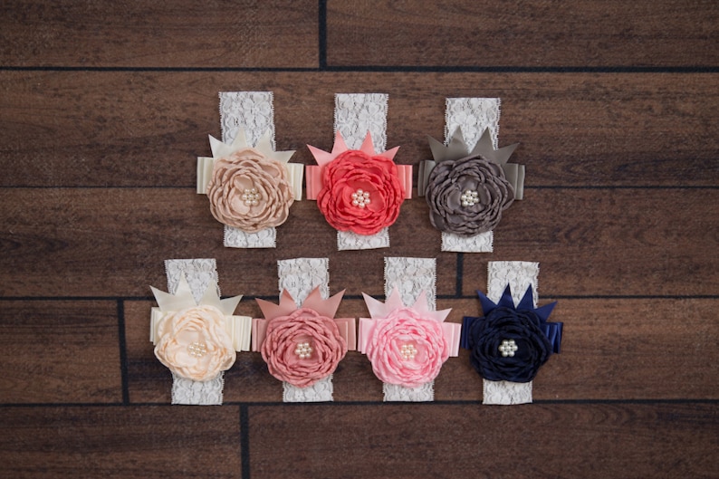 May include: Seven white lace headbands with different colored fabric flowers. The flowers are peach, coral, pink, gray, and navy blue. Each flower has a pearl in the center.