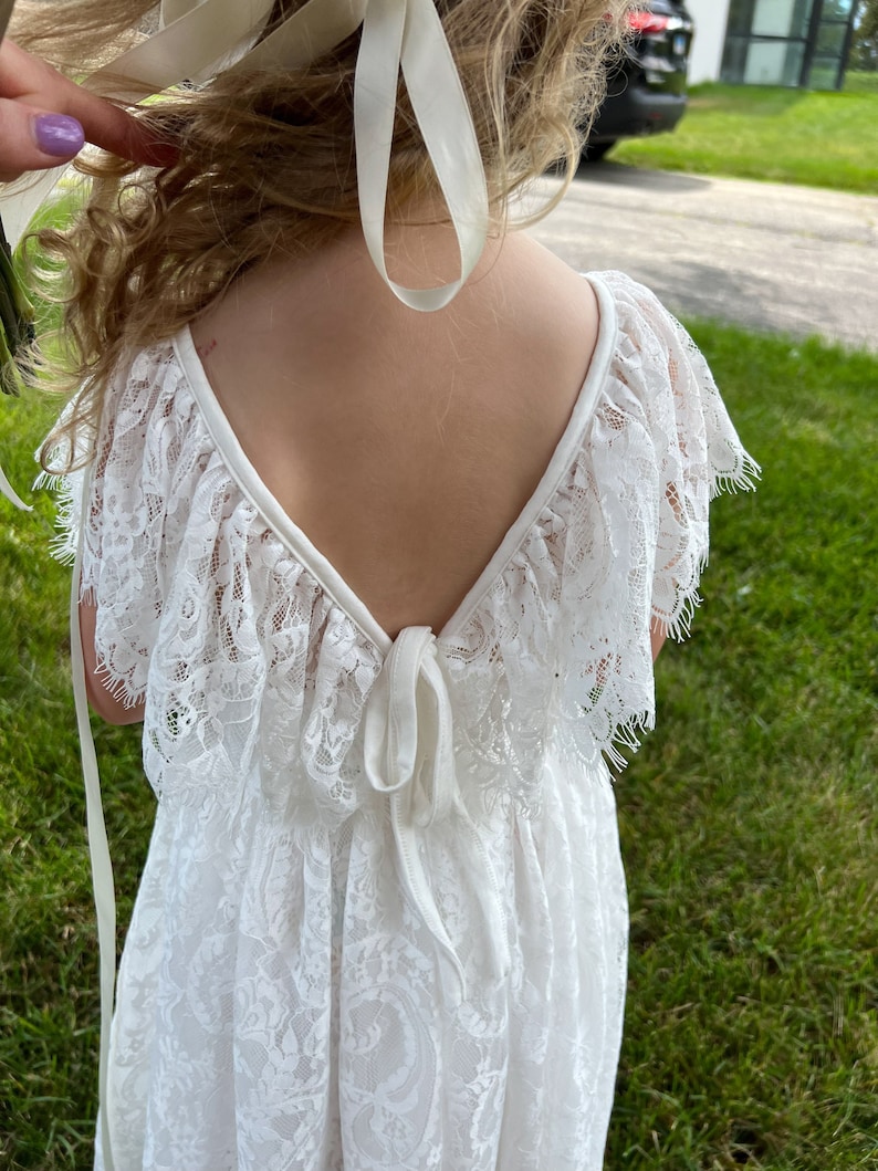 May include: White lace dress with a V-neck back and a tie at the waist.