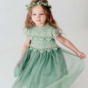 May include: A young girl wearing a sage green tulle dress with lace detailing and a leafy green flower crown.