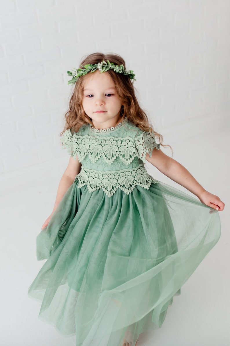 May include: A young girl wearing a sage green tulle dress with lace detailing and a leafy green flower crown.