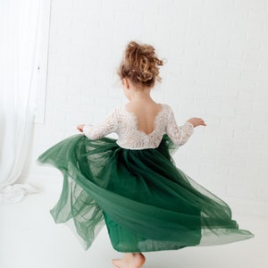 Pu&ograve; includere: Un abito con corpetto in pizzo bianco a maniche lunghe con scollo profondo sulla schiena e un'ampia gonna in tulle verde scuro. La gonna &egrave; ritratta in movimento, creando una forma circolare ampia che si apre a ventaglio dalla vita.