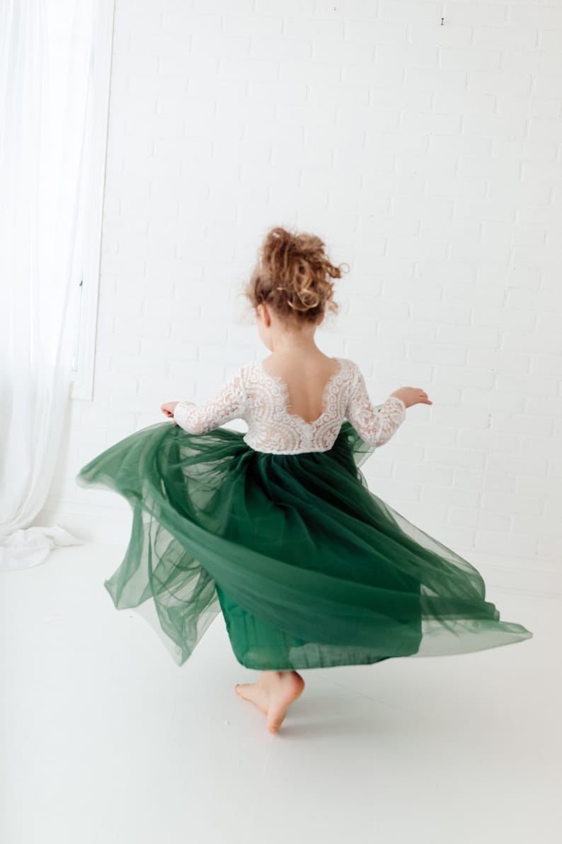 Pu&ograve; includere: Un abito con corpetto in pizzo bianco a maniche lunghe con scollo profondo sulla schiena e un'ampia gonna in tulle verde scuro. La gonna &egrave; ritratta in movimento, creando una forma circolare ampia che si apre a ventaglio dalla vita.