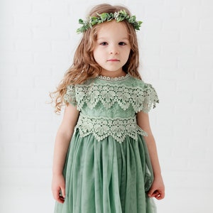 May include: A young girl wearing a sage green tulle dress with lace detailing and a green leaf crown.