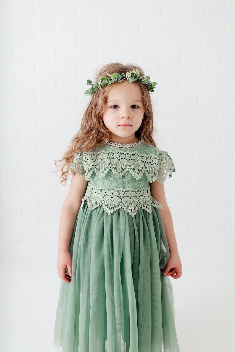 May include: A young girl wearing a sage green tulle dress with lace detailing and a green leaf crown.