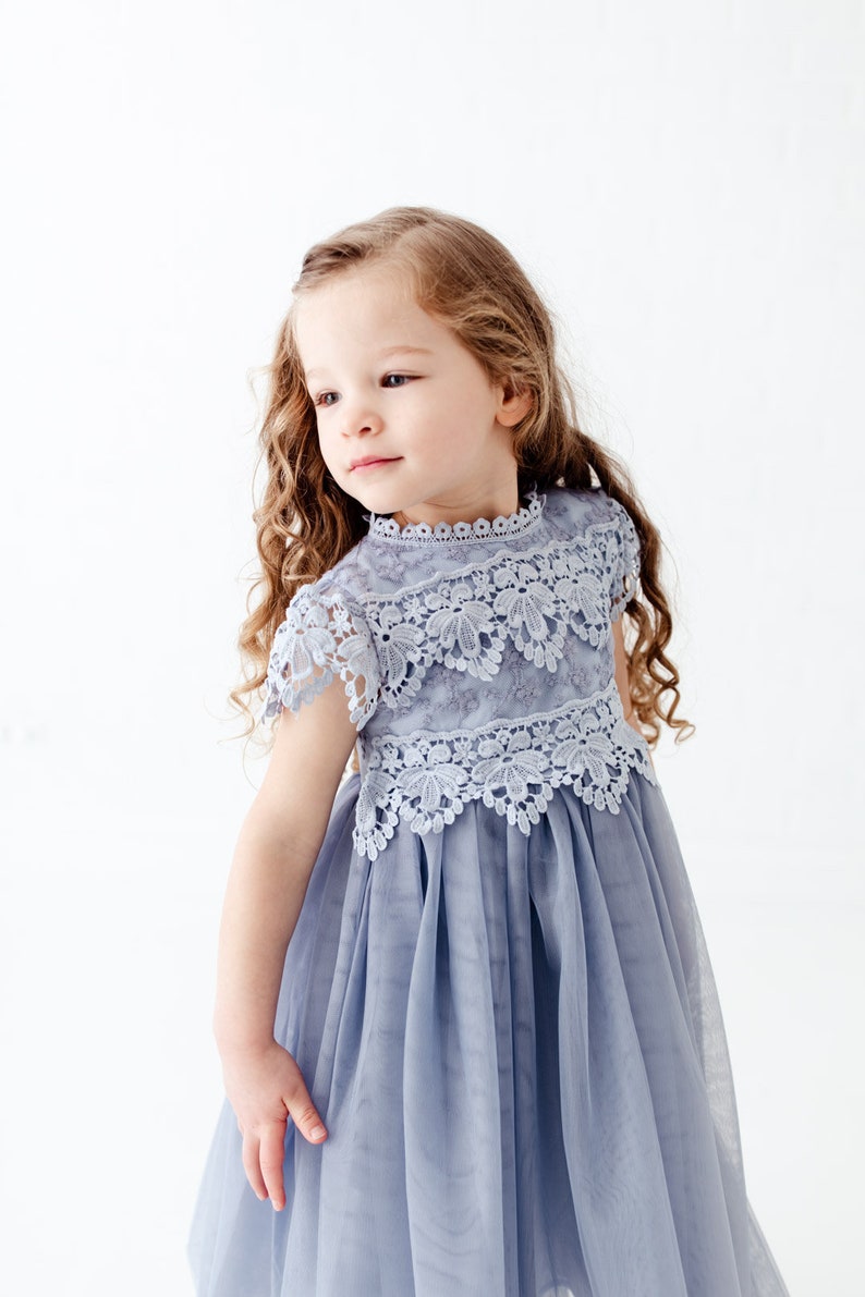 K&ouml;nnte beinhalten: Ein junges M&auml;dchen tr&auml;gt ein hellblaues T&uuml;llkleid mit einem Spitzenoberteil. Das Kleid hat einen runden Ausschnitt und kurze &Auml;rmel. Das M&auml;dchen hat lange, lockige braune Haare.