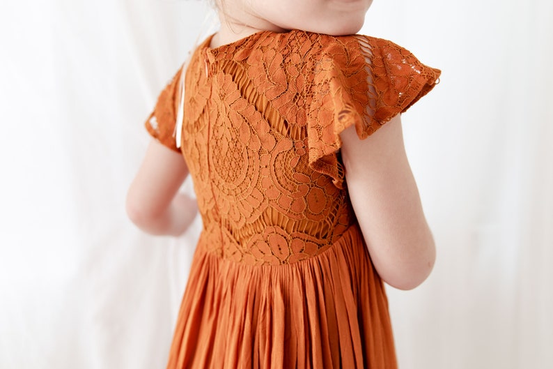 Op de afbeelding: Een roestkleurige kanten jurk met korte mouwen en een geplooide rok.