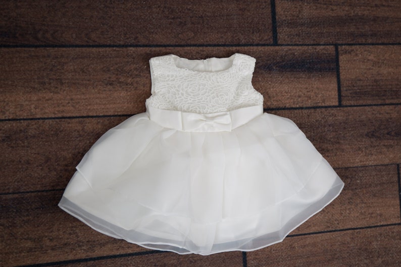 Puede incluir: Un vestido de tul blanco con un corpi&ntilde;o de encaje y un lazo de sat&eacute;n. El vestido tiene una falda de capas y es perfecto para una ocasi&oacute;n especial.