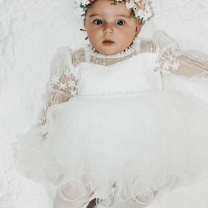 K&ouml;nnte beinhalten: Ein kleines M&auml;dchen tr&auml;gt ein wei&szlig;es T&uuml;llkleid mit Blumenstickerei und einer Blumenkrone. Sie tr&auml;gt wei&szlig;e Strumpfhosen und silberne Schuhe.