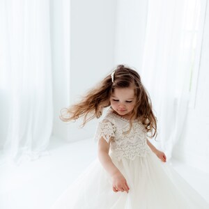 May include: A young girl twirls in a white dress with a lace bodice and flowing tulle skirt. Her long, light brown hair is styled with a pearl hair clip. The dress is perfect for a special occasion.