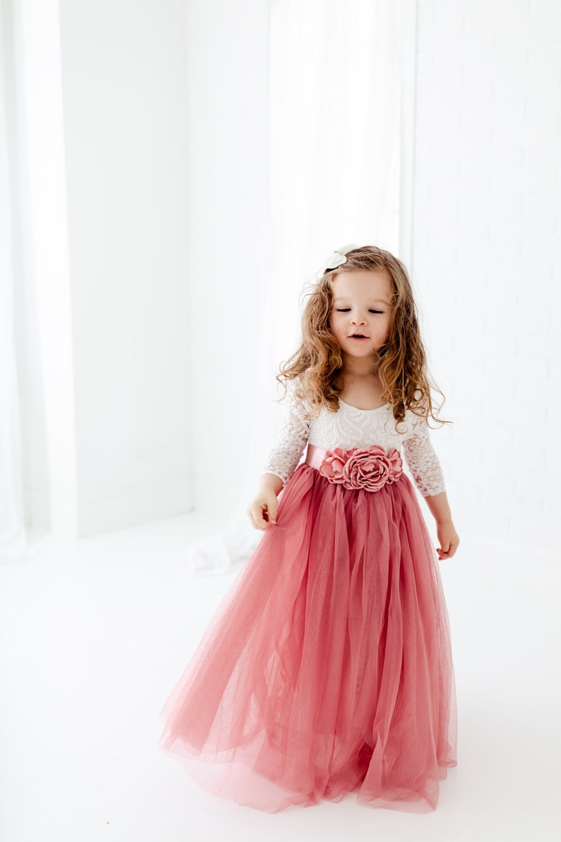 May include: A young girl wearing a white lace top with a pink tulle skirt and a large pink flower accent at the waist.
