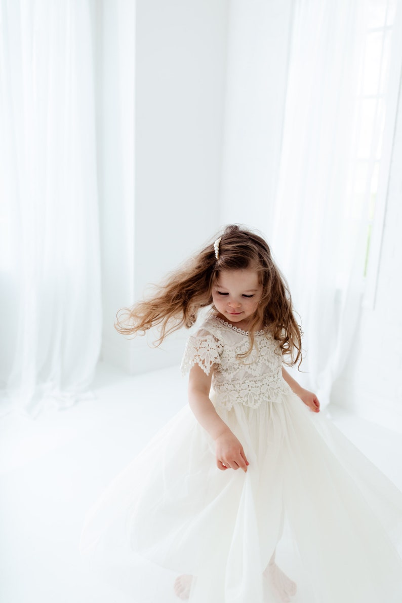 Op de afbeelding: Een jong meisje draagt een witte kanten jurk met een tule rok. Ze draait rond en haar haar waait.