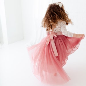 May include: A young girl wearing a white lace top and a dusty pink tulle skirt with a matching satin ribbon. The skirt is flowing and the girl is twirling.