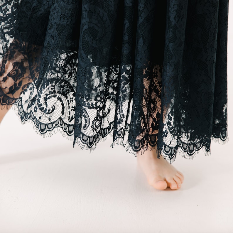 May include: A dark navy blue lace skirt featuring an intricate floral pattern throughout the fabric. The hemline is finished with a scalloped edge that displays delicate, fine fringe detailing along the bottom of the garment.