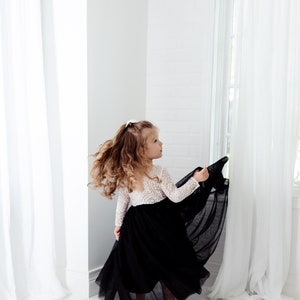 May include: A floor-length dress featuring a white long-sleeved lace bodice with a scoop back and a voluminous black tulle skirt. The garment has a fitted waistline where the intricate white lace meets the layered, flowing black tulle fabric.