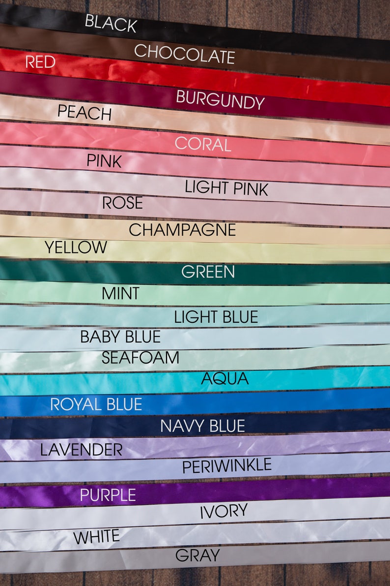 May include: A collection of satin ribbons arranged in horizontal rows, each labeled with its color: black, chocolate, red, burgundy, peach, coral, pink, light pink, rose, champagne, yellow, green, mint, light blue, baby blue, seafoam, aqua, royal blue, navy blue, lavender, periwinkle, purple, ivory, white, and gray.