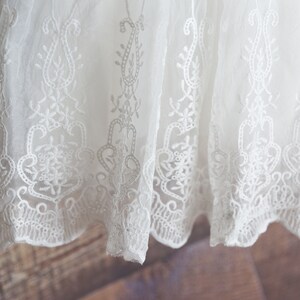 May include: White lace fabric with a delicate floral pattern. The lace has a scalloped edge.