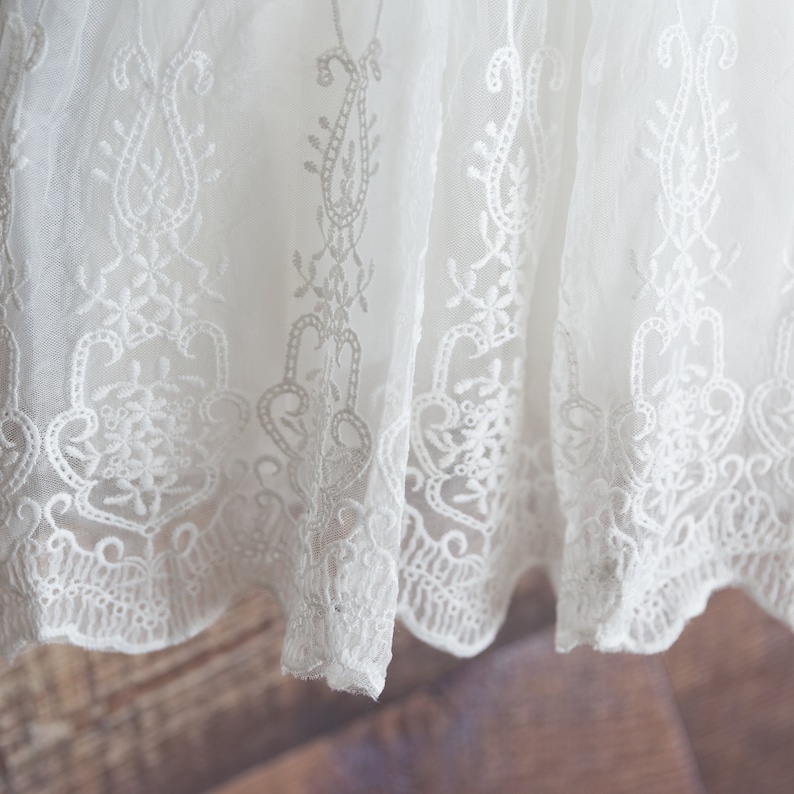 May include: White lace fabric with a delicate floral pattern. The lace has a scalloped edge.