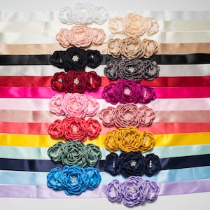 Pode incluir: Um conjunto de 12 fitas de cetim em v&aacute;rias cores, cada uma com um enfeite de tr&ecirc;s flores. As flores s&atilde;o feitas de tecido e t&ecirc;m detalhes de p&eacute;rolas.