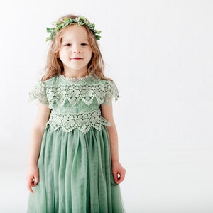 May include: A young girl wearing a sage green tulle dress with lace detailing and a green leaf crown.