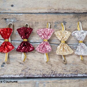 May include: Five sequined bow ties in different colors: red, burgundy, pink, gold, and silver. The bow ties are attached to elastic bands.