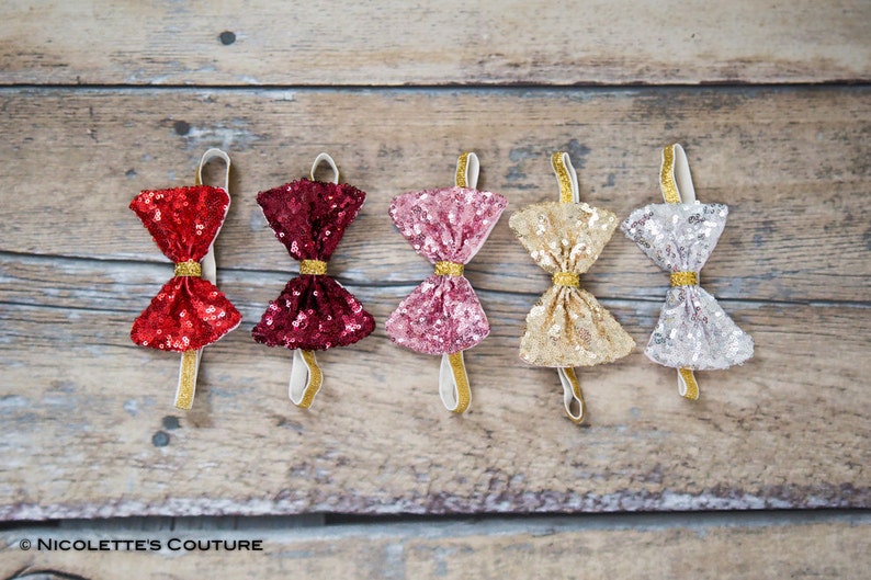 May include: Five sequined bow ties in different colors: red, burgundy, pink, gold, and silver. The bow ties are attached to elastic bands.