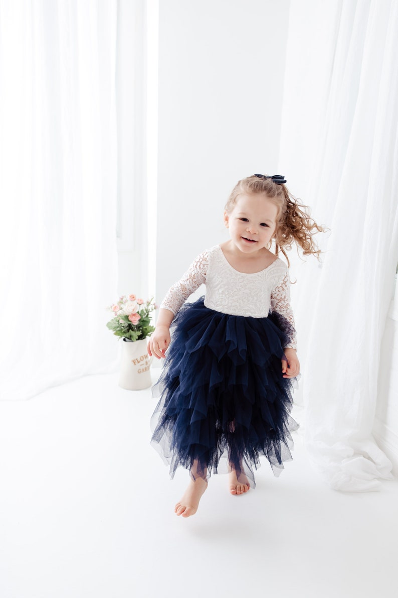 May include: A dress featuring a white lace bodice with three-quarter length sleeves and a voluminous, layered navy blue tulle skirt. The garment has a scoop neckline and a fitted waistline, with the skirt falling to a mid-calf length.