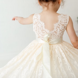 May include: A white lace dress with a satin ribbon sash. The dress has a scoop neckline and a sleeveless design. The back of the dress features a lace panel.