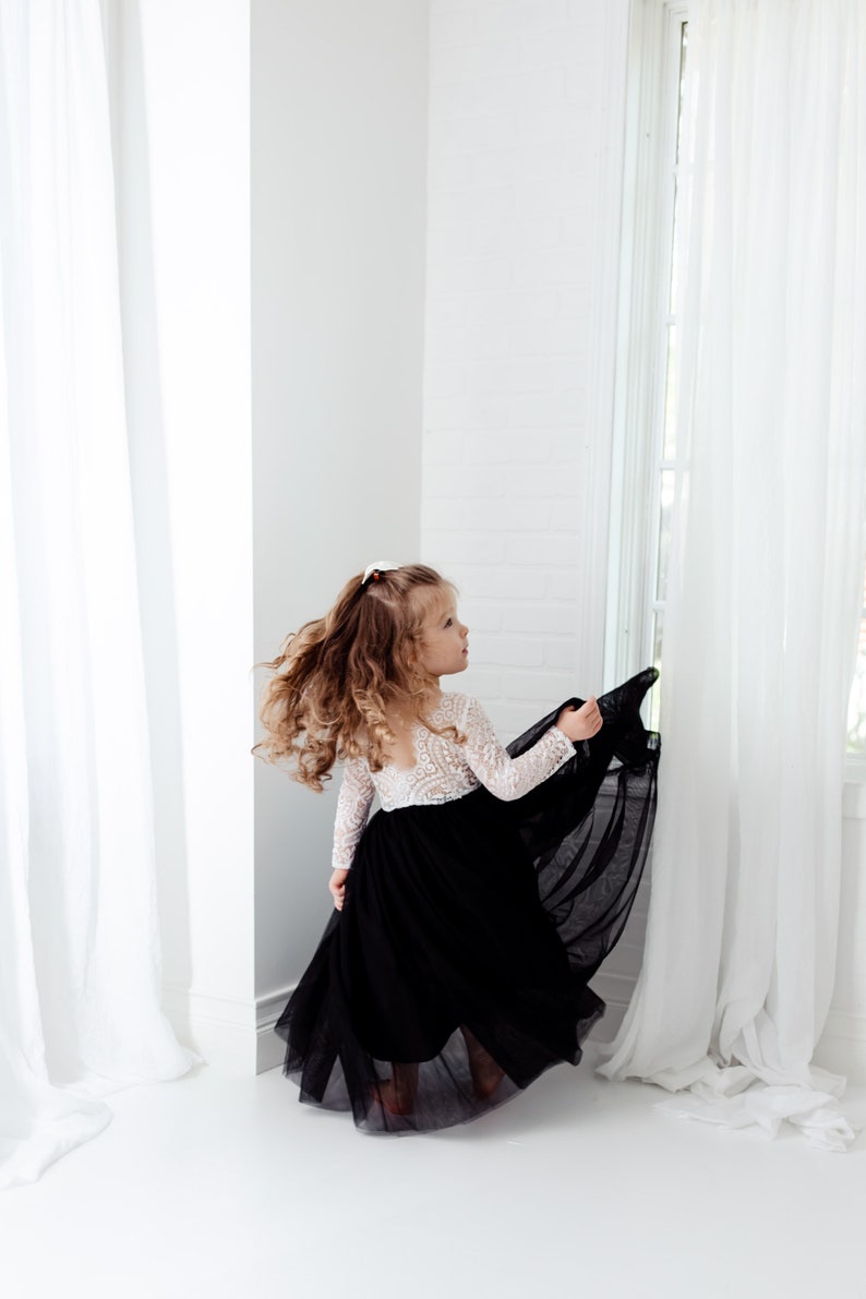 May include: A dress featuring a white long-sleeved lace bodice with a scoop neckline and a floor-length black tulle skirt. The garment has a fitted waistline where the intricate white lace meets the voluminous, layered black tulle fabric.