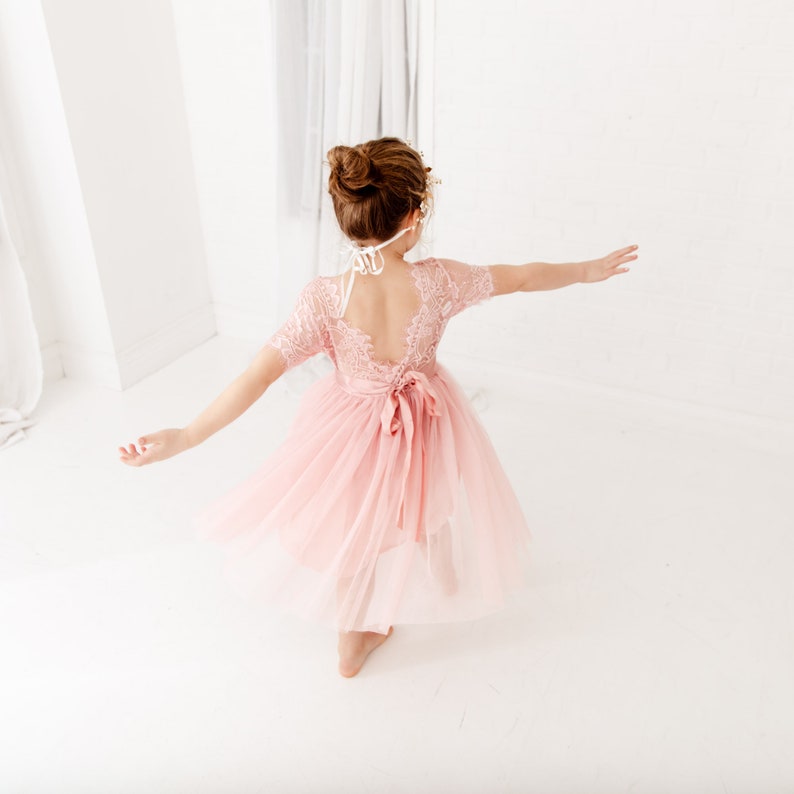 Pode incluir: Uma menina pequena vestindo um vestido de tule rosa com detalhes em renda e uma fita branca. O vestido tem costas abertas e &eacute; perfeito para uma ocasi&atilde;o especial.