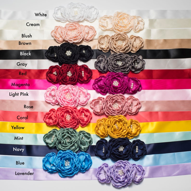 May include: A collection of satin ribbons, each featuring three fabric flowers adorned with central faux pearls. The ribbons are displayed in various colors including white, cream, blush, brown, black, gray, red, magenta, light pink, rose, coral, yellow, mint, navy, blue, and lavender, with each color name printed next to its corresponding ribbon.