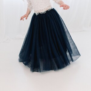 May include: A navy blue tulle skirt with a full, flowing silhouette. The skirt is made of soft, delicate fabric and has a gathered waistband.