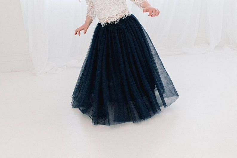 May include: A navy blue tulle skirt with a full, flowing silhouette. The skirt is made of soft, delicate fabric and has a gathered waistband.