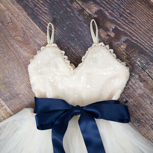 May include: A white tulle dress with a sequined bodice and a navy blue satin ribbon tied around the waist.