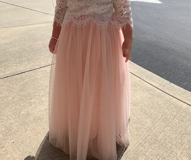 May include: A pale pink tulle skirt with a white lace top. The skirt is long and flowing, and the top has a delicate lace pattern.