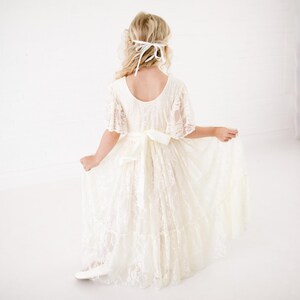 以下が含まれることがあります： 白いレースのドレスにサテンのリボンと白いヘッドバンドが付いている。ドレスはゆったりとしたスカートで、特別な機会に最適です。